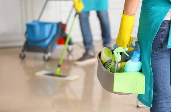 Cleaner holding a caddy of cleaning supplies while a teammate mops the floor